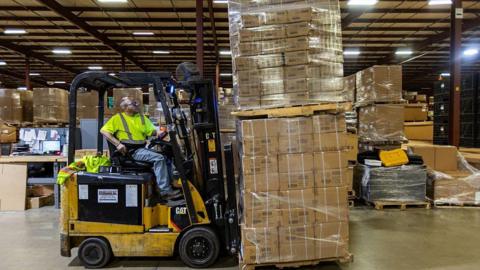 A person in a yellow reflective vest mans a forklift piled high with boxes of toys at the Duncan Toy Company in the firm's warehouse in Columbus, Indiana, on April 16, 2025. 