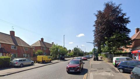 Google Streetview image of Bell's Lane, a wide residential street of two storey post war brick houses, with cars parked on either side