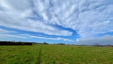 Bright blue sky filled with swirling clouds and a bright green field in the foreground