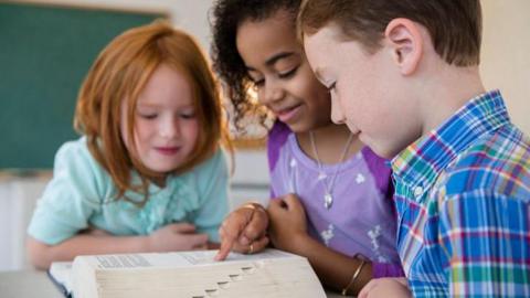 Three children looking at a dictionary.