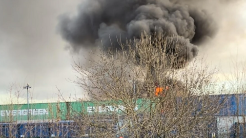 A large black cloud of smoke is coming from a fire in the industrial area