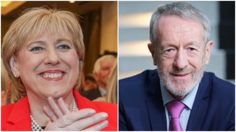 A blonde haired woman in red claps her hands, while a grey haired man is on the right and wears a purple tie.
