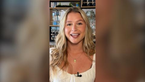 Mollie Pearce smiles in a bar. She has long wavy blonde hair and wears a white top
