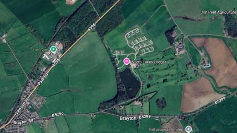 A Google Maps screenshot showing an aerial view of the location where North Lakes Lodges is. It is on a parcel of land between the A596 and the B5299. The area is mostly surrounded by green space.