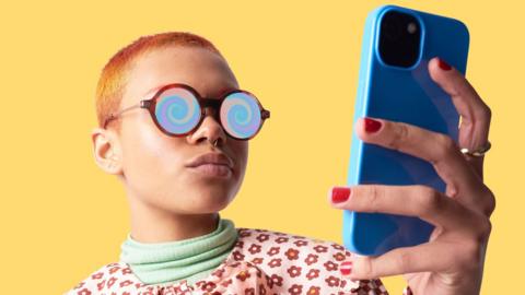 Woman with short hair wearing glasses with a spinning vortex on the lenses, looking at a mobile phone.