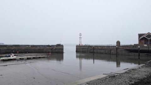 A grey sky reflects down onto grey water at Newhaven Harbour.