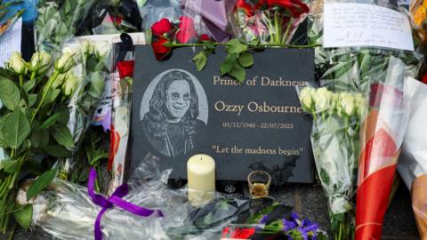 Flower tributes for Ozzy Osbourne in front a plaque that says Prince of Darkness, Ozzy Osbourne. 