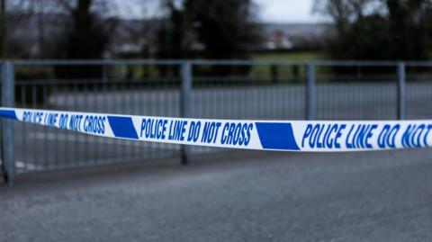 Blue and white police tape is stretched across a crime scene with concrete walls in the background