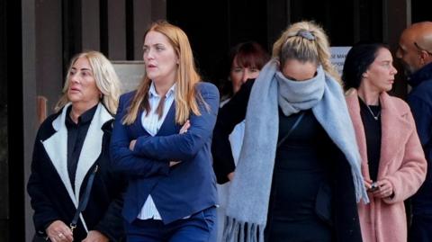 Danielle Dowdall leaving court with a light blue scarf covering her face, with Roxanne Matthews who has a blue blazer and has her arms crossed 