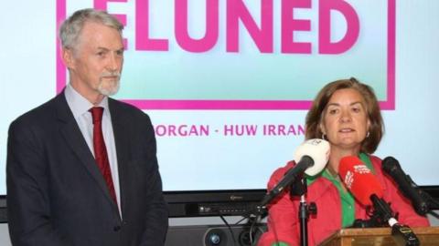 Huw Irranca-Davies and Eluned Morgan on a stage in front of a screen showing their names