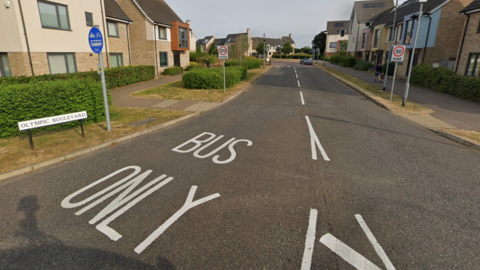 A road with the words "bus only" painted on it. There are houses on either side and a sign with the road name: "Olympic Boulevard."