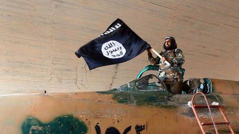 A bearded man waves an Islamic State black flag from the cockpit of a plane