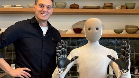 A smiling man pictured next to a domestic robot in a kitchen