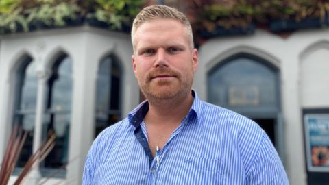 A man in a blue and white striped shirt looks at the camera