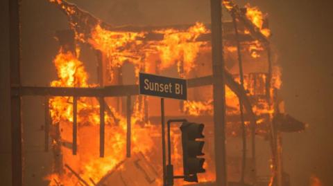 Flames from the Palisades Fire burn a building on Sunset Boulevard amid a powerful windstorm on 8 January, 2025.