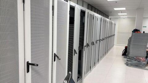 A row of locker doors at a date centre. They are predominantly grey in colour with black handles. 