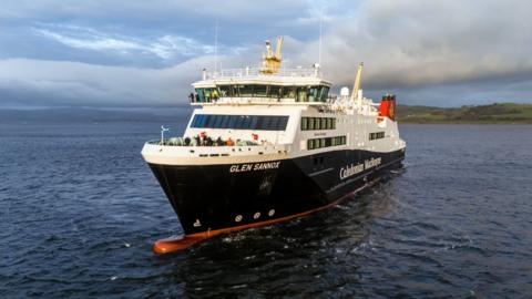 Glen Sannox, a black and white ship with red funnels, sailing towards the camera in the Firth of Clyde, with hills in the background