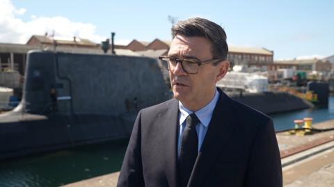 Andy Burnham during interview next to a submarine