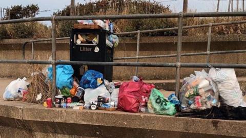 Carrier bags full of litter are piled up next to a bin on Skegness promenade