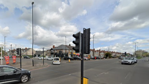 A junction showing a street going from left to right, Ansty Road, with a traffic light prominent in the middle of the photo. Another road, Sewall Highway, is at an angle on the left of the image. 