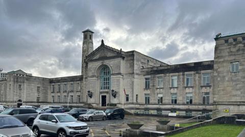 The outside of Southampton city council officers with white and dark clouds behind. The car park out the front is full with cars. 