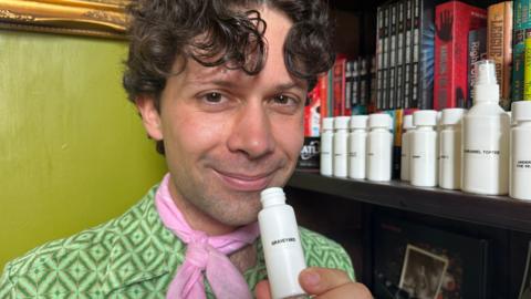 A man with curly hair wearing a green shirt and pink neck tie. 