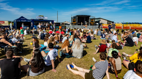 Sluagh nan suidhe air an fheur aig Fèis Chiùil Thiriodh air là ghrianach