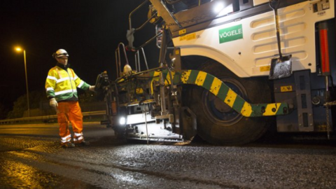 A man in high-vis clothing stands next to a large tarmac-laying vehicle