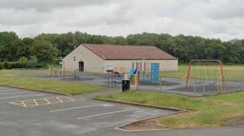 A football changing room building next to a play area and car park