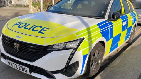 A Devon and Cornwall Police car parked up on a road. A silver Ford Mondeo is parked behind it. The police car is a Peugeot and has the licence plate WA72 EBG.
