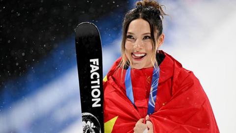Eileen Gu with her silver medal around her neck, wrapped in a Chinese flag