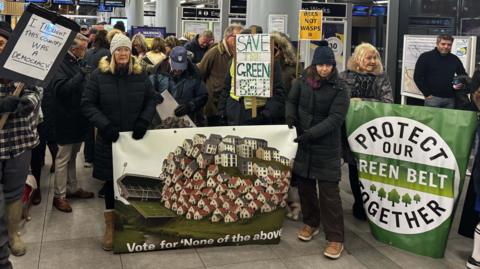 Protestors gather in the concourse of Sevenoaks train station with banners about protecting the green land