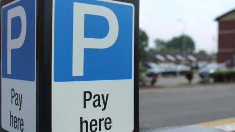 A display which has a giant white letter P on a black background and pay here written underneath, it is a parking sign