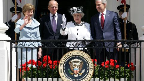 Queen Elizabeth II standing on a balcony alongside President George Bush, Prince Phillip and Laura Bush.