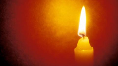 A white wax candle burning with a bright yellow flame with an orange glow around it.