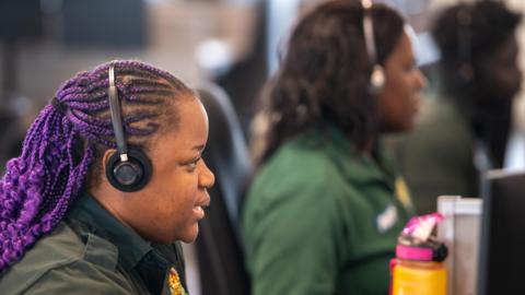 An image of two ambulance dispatchers in a call centre. They are wearing headsets and dark green clothing.