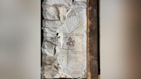 Faded painting of a red flower with a green stem on a wall. There are red lines above and below and in the middle of the flower. 