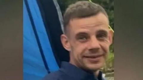 Rikki Berry, 36, with short hair wearing a blue shirt and smiling at the camera 