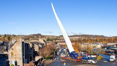 A giant wind turbine blade on the back of a special lorry travels through the centre of Hawick holding up traffic on its way