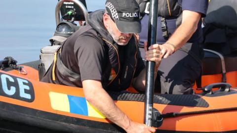 A man in a police cap searching the water with a black pole