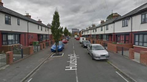 Google Maps image of Hudson Street in Cheltenham. Houses are lining both sides of the street and cars are parked. 