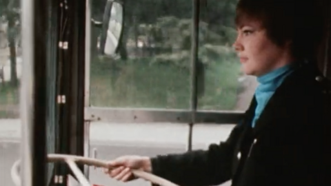 Sandra Holt the UK's first female bus driver holds steering wheel of bus