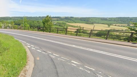 A google maps image of the A30, with fields either side of the road and woodland in the distance