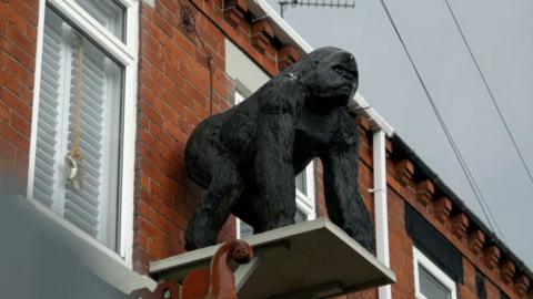 A statue of a gorilla stands on a platform attached to the top story of a terraced house
