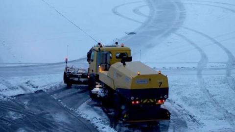 A snow plough waits to help clear snow from around aircraft after overnight snowfall caused the temporary closure of Manchester Airport.