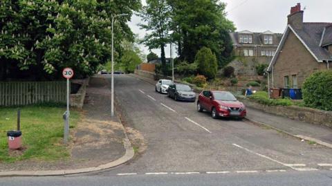A Google street view image of a residential street with cars parked at the side of the road