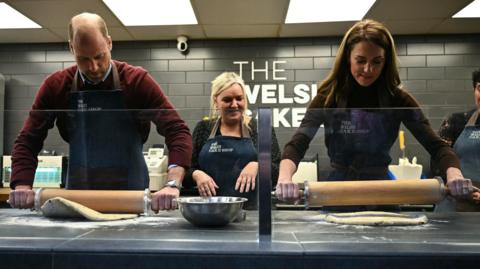 The Prince and Princess of Wales help prepare and cook a batch of Welsh cakes at the Welsh Cake Shop as shop owner Theresa Connor (centre), looks on, during a visit to Pontypridd Market in Wales to talk to local business owners about the impact of the flooding caused by Storm Bert and Storm Darragh