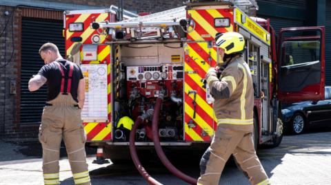 Fire engine and fire fighters attending a fire in a public car park.