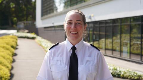 Woman with brown hair in a bun in police uniform - white shirt, black tie and shoulder pads 