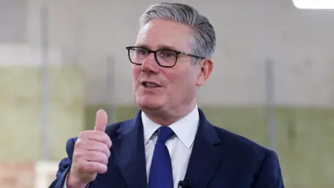 Starmer gestures with right hand while speaking in front of two microphones